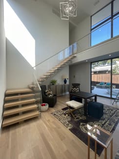 White oak floating treads with glass railing climb to a bridge in a sunlit double-height living room.