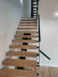 Thick white oak treads on a black mono stringer with frameless glass and black handrail in a narrow stairwell.