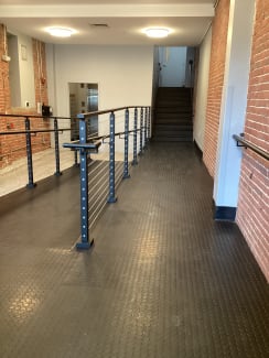 Black cable railing with handrails runs along a ramp in a brick-walled commercial corridor.