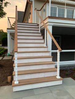 White intermediate posts with stainless cables and a wood handrail follow a long exterior stair to a porch.