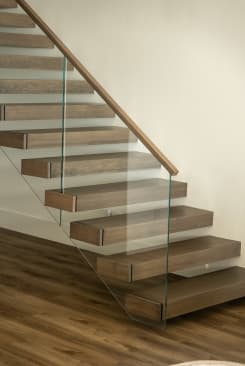 Brown oak cantilever treads off a white wall with frameless glass guard and a wood handrail.