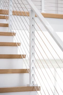 Close view of a white post with cable infill beside natural oak treads on white risers.
