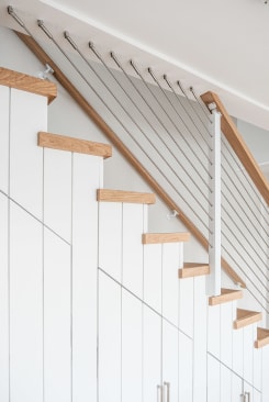 Stainless cable infill and a light oak handrail along white shiplap stairs with oak treads.