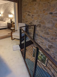 Black cable railing with walnut handrail edges a carpeted loft against a rustic stone wall.