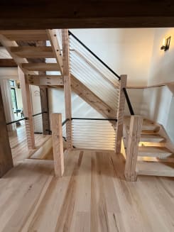 Rustic timber stair with chunky wood newels and black cable railing climbing to a landing.