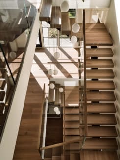 Looking down a multi-level stairwell of wood floating treads with glass railing and clusters of globe pendant lights.