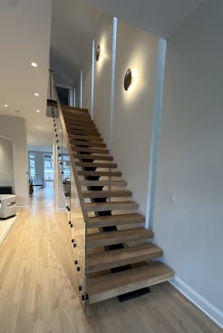 Long straight white oak floating stair with frameless glass beside warm wall sconces