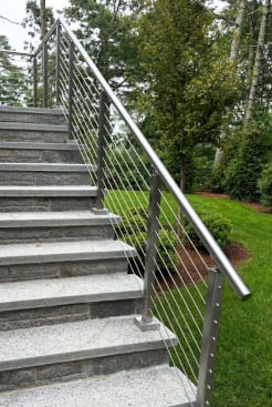 Brushed stainless posts with a 2-inch round handrail and cable infill climbing a long granite garden stair.