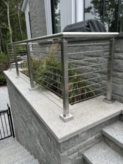 Brushed stainless posts and round handrail with cable infill along granite entry steps and a planter wall.
