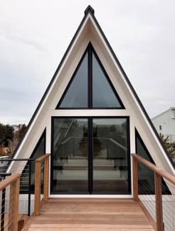 Cable railing with wood posts and cap frames an Ipe deck leading to a modern A-frame glass facade.