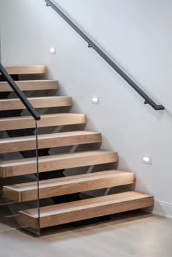 Thick white oak floating treads with a glass railing and a black metal wall-mounted handrail that returns into the wall.