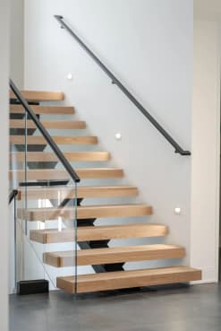 White oak floating treads on a hidden mono stringer with glass railing and a black wall handrail with wall returns.