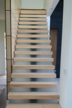 Thick maple treads cantilevered from a paneled wall seen straight up the flight.