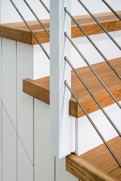 Close view of a white slim side-mount cable post fastened to a stair stringer with oak treads.