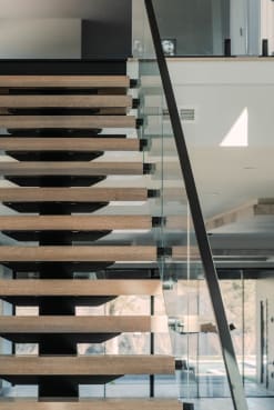 Looking up beneath oak treads on a black mono stringer with standoff-pin glass and a handrail.