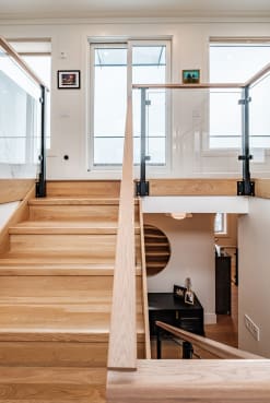 Ash wood stair with a matching wood handrail and post-to-post glass railing at the landing.
