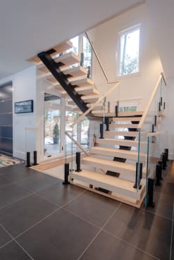 Light oak treads on black mono stringers with glass between black posts at a switchback landing.