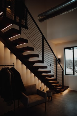 Dark floating treads with under-tread LEDs on a mono stringer with black rod railing in a moody entry.