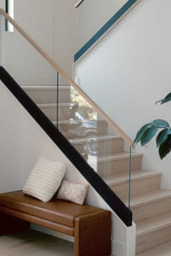 Frameless glass in a black base channel with a light wood handrail along a closed oak stair above a leather bench.