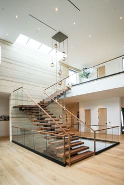 Walnut floating treads switch back beneath a skylit atrium with frameless glass, wood handrails and cascading glass pendants.