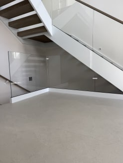 Frameless glass encloses the area beneath a white-stringer floating stair over a terrazzo floor.