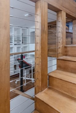 Stainless horizontal rods run between warm wood posts beside a natural wood stair.