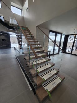 Walnut floating stair treads on a black center stringer with Vedera glass railing and a wood handrail, treads still wrapped in protective covers