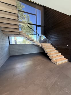 Floating white oak stair with frameless glass rising past a window wall in a dark-paneled entry