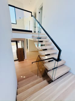 Looking down an oak floating stair with frameless glass and a black flat handrail.