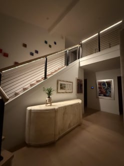 Black cable railing with a wood handrail glowing with integrated LED light runs up a stair and along a balcony.