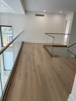 Frameless glass railing with a brass handrail edges an upper hallway and stair opening on white oak flooring.