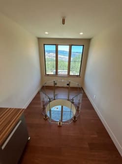 Octagonal glass railing ring around a round floor opening at the end of a long wood-floored hallway with a view window.