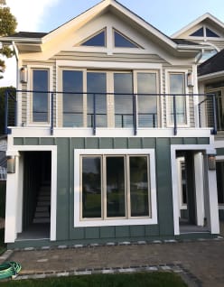 Black cable railing spans an upper balcony across a cream-and-green lake house facade.