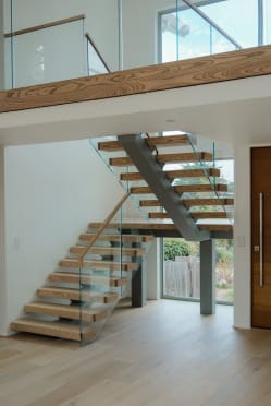 Rustic wood treads on a gray mono stringer turn at a mid landing with glass railing and wood handrail.