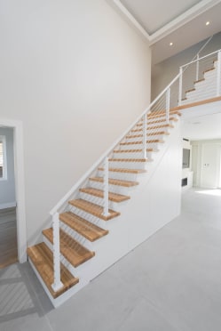 Oak treads and white cable railing rise along a tall white wall to a second-floor landing.