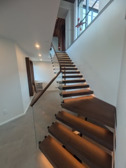 Walnut floating treads with LED lights and frameless standoff glass rising past a window