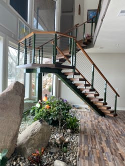 Dark stringer floating stair with wood treads and cable railing rises above an indoor rock garden.