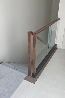 Frameless base rail glass with a walnut cap and squared walnut newel at the head of a stair