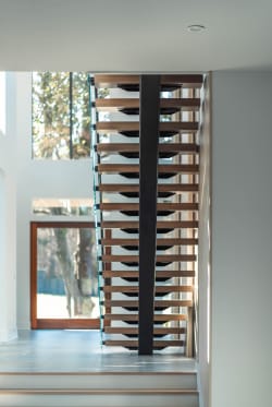Straight-on view of a black center stringer with oak treads framed by tall windows and a wood door.