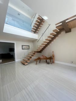 Wood floating treads on a wood-clad mono stringer climb past glass railing to a glass-railed loft.