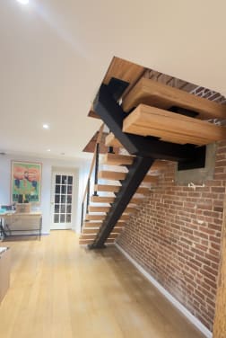 Black mono stringer and thick white oak treads rising along an exposed brick wall