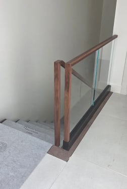 Frameless base rail glass with a walnut cap and squared walnut newel at the head of a stair