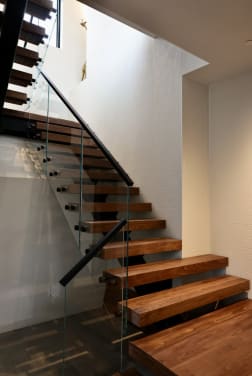 Thick walnut treads float beside frameless glass panels with black standoffs and a black handrail.