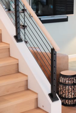 A black cable post cut down onto an angled knee wall with a maple handrail along an oak stair.