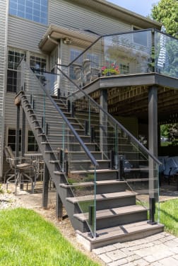 Composite deck and stair on a two-story home with frameless glass panels on black talons and a black handrail.