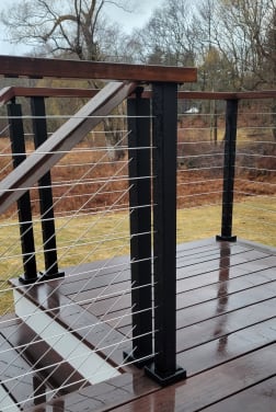Black cable posts with an Ipe cap rail along a rain-wet hardwood deck and stair.