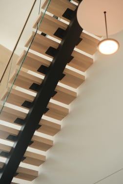 Upward view of white oak treads on a black mono stringer with a glass railing and a round pendant light.