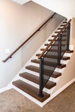 Dark stained thick-nose replacement treads with white risers pair with a black perforated panel railing and wall handrail.