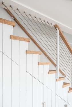 Stainless cable infill and a light oak handrail along white shiplap stairs with oak treads.