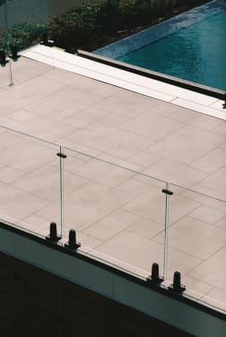 Frameless glass panels on black talon spigots edging a stone pool terrace.